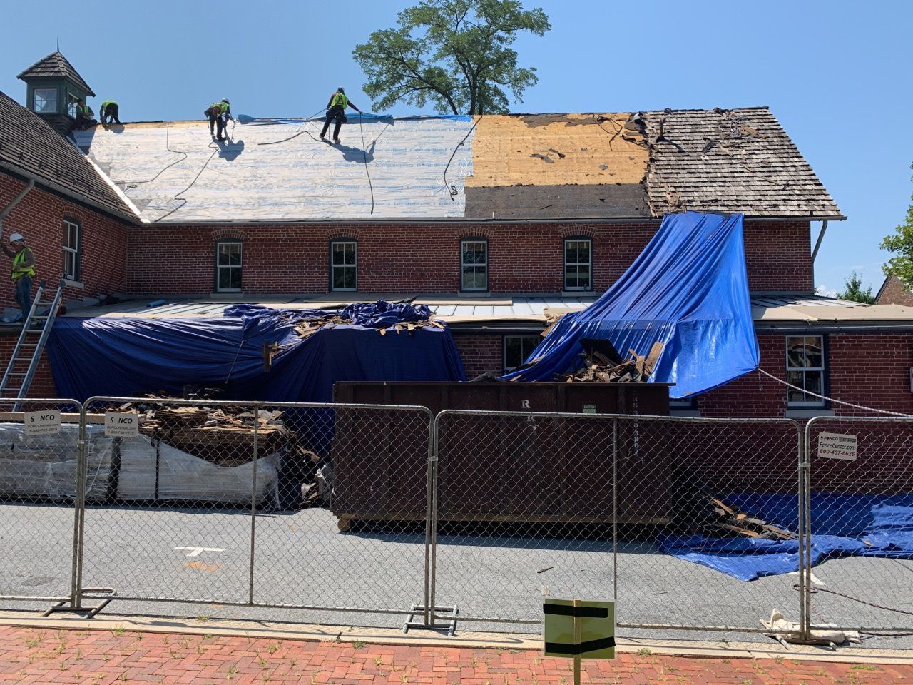 Damaged building with tarps and a chain-link fence in front, under repair after storm damage