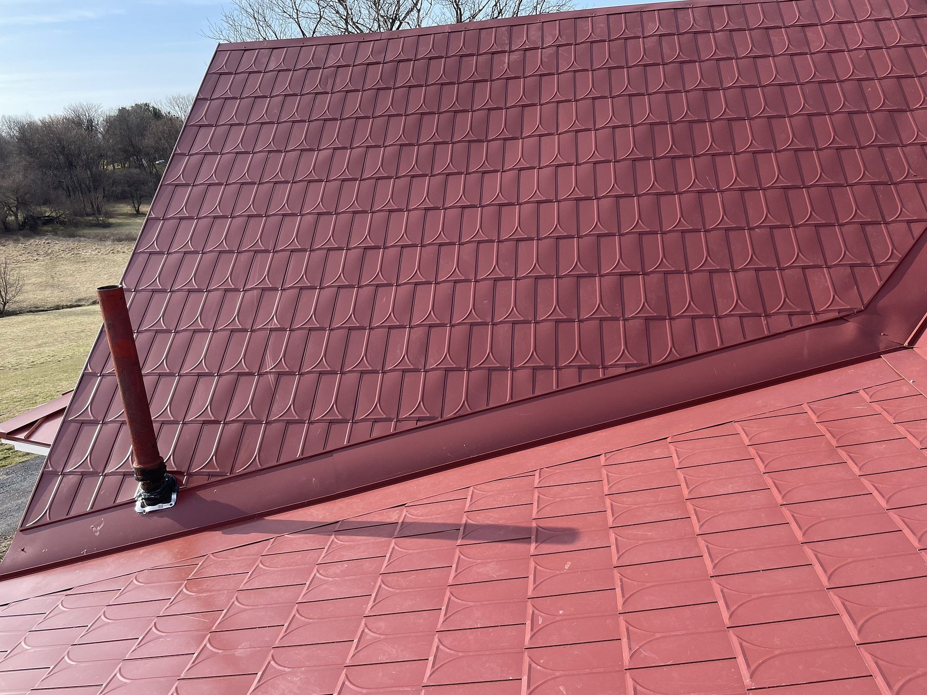 Red metal roof with a chimney against a blue sky, outdoors.