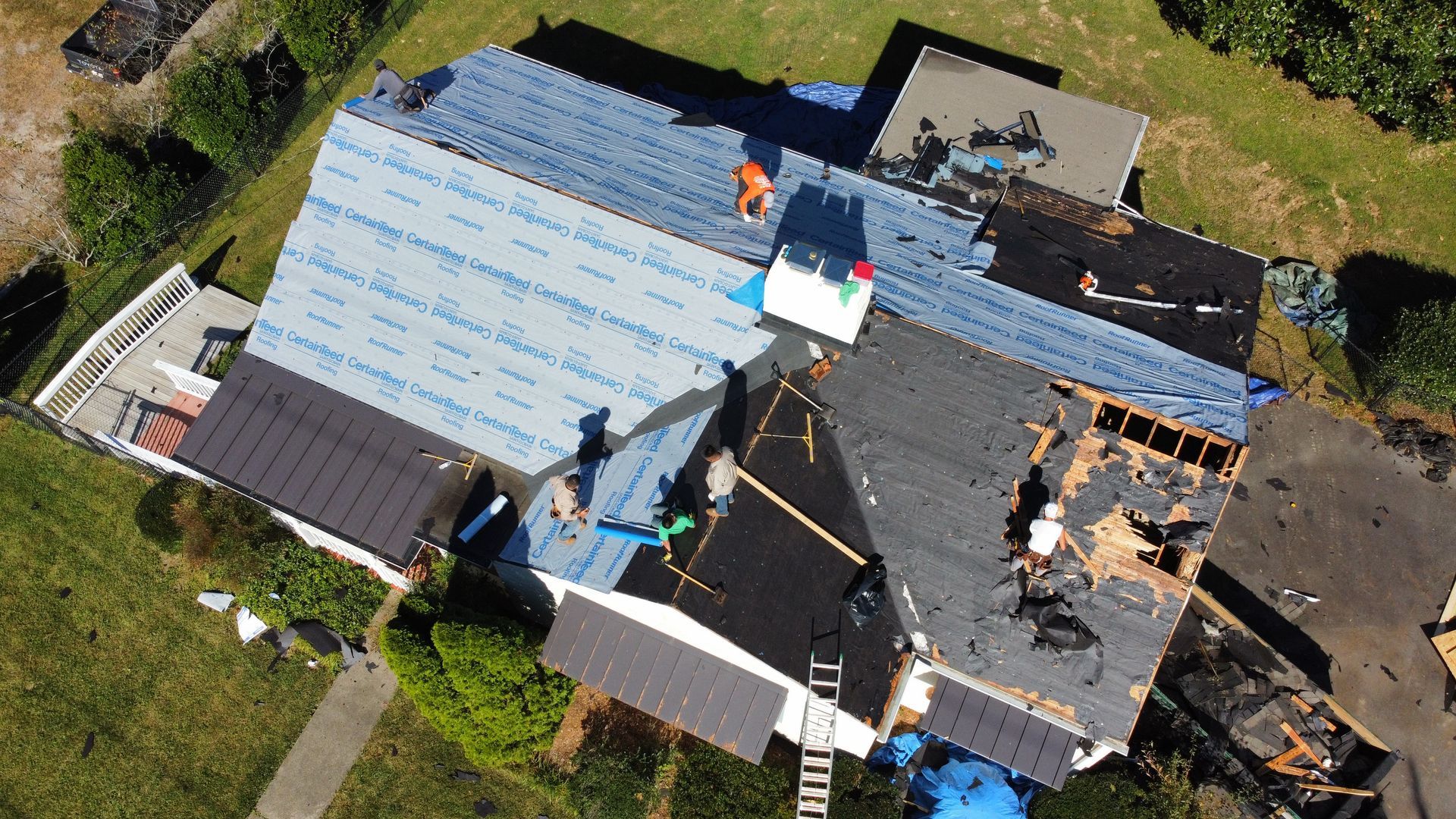 Aerial view of a roof undergoing repairs, with exposed underlayment and workers on the house.