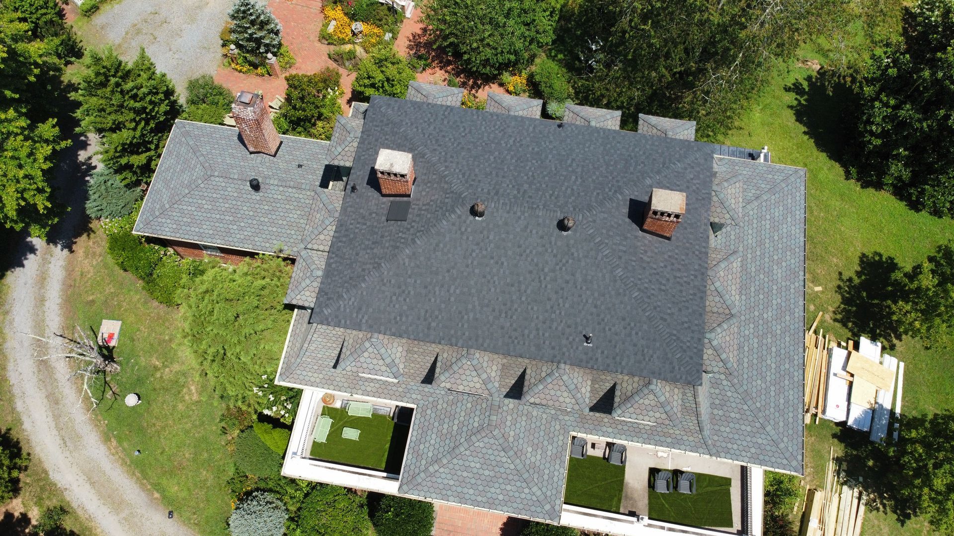 Aerial view of a gray-roofed house surrounded by green trees and lawn