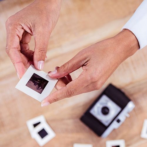 Hands holding a small instant photo over a table with scattered photo prints and a camera nearby