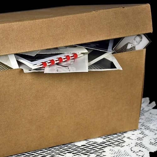 Cardboard box stuffed with papers and envelopes, lid ajar on a lace-covered surface.