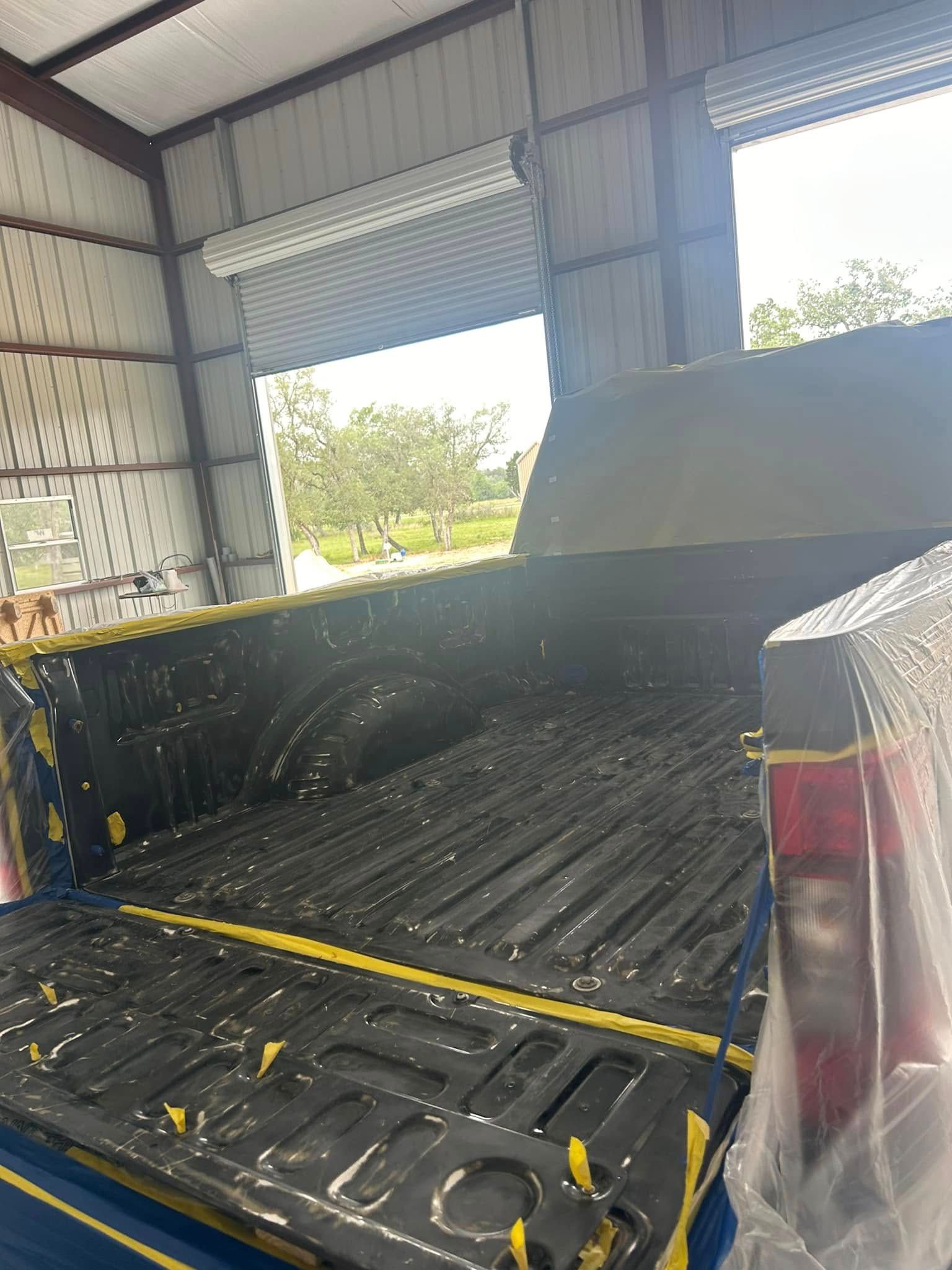 The back of a truck is being painted in a garage.