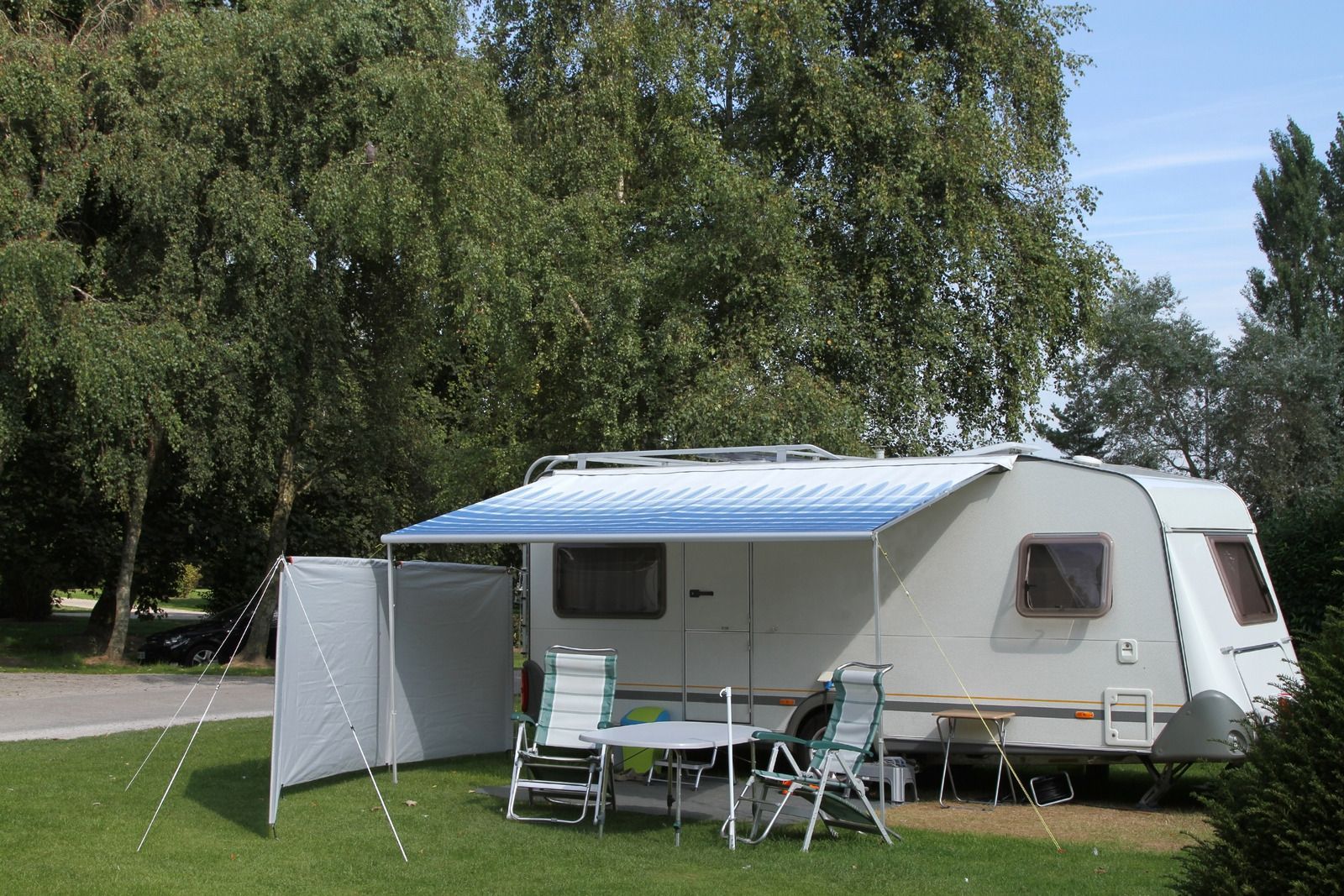 A caravan with a blue awning is parked in a grassy field.