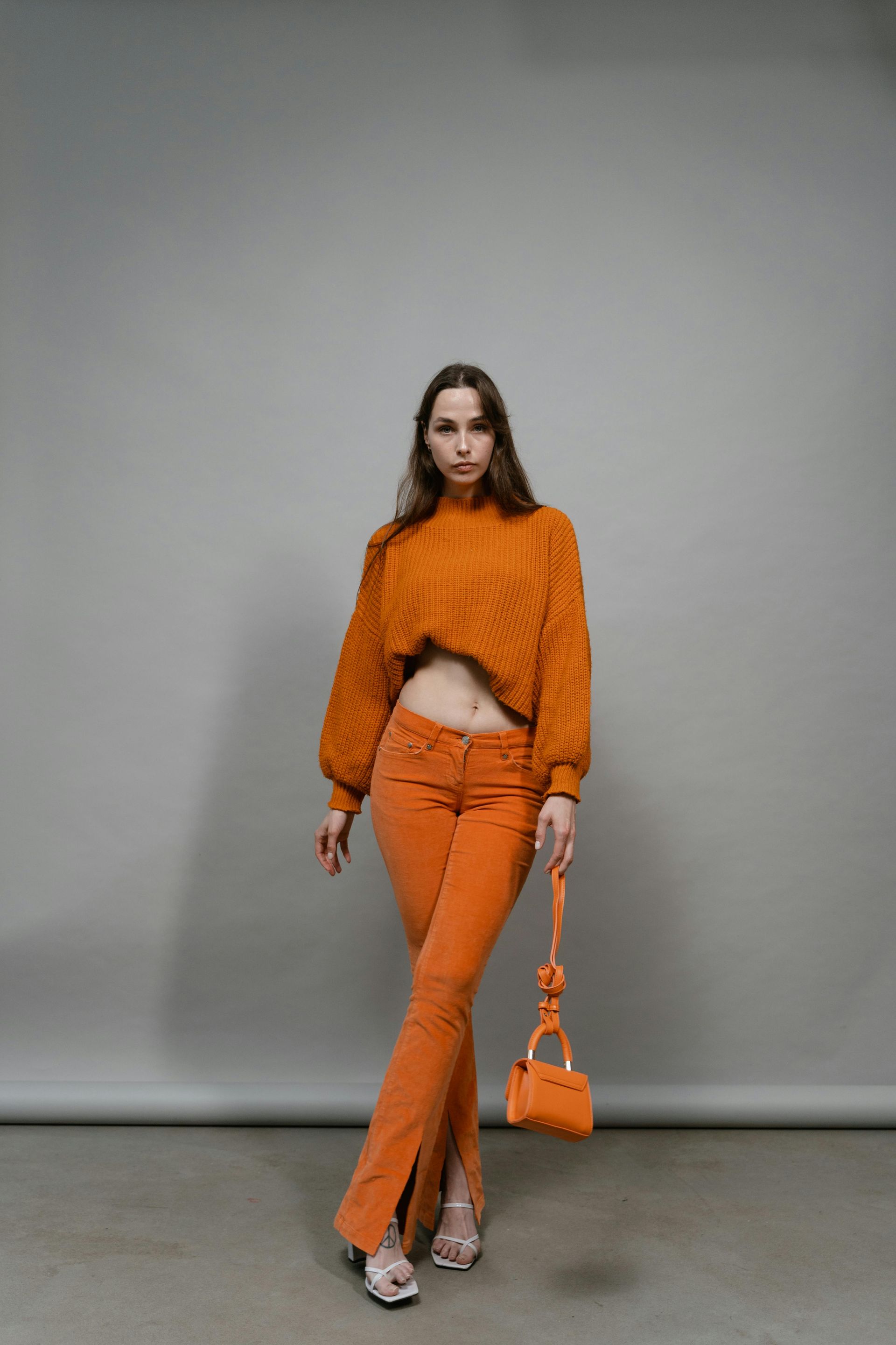 A woman in an orange sweater and orange pants is holding an orange purse.