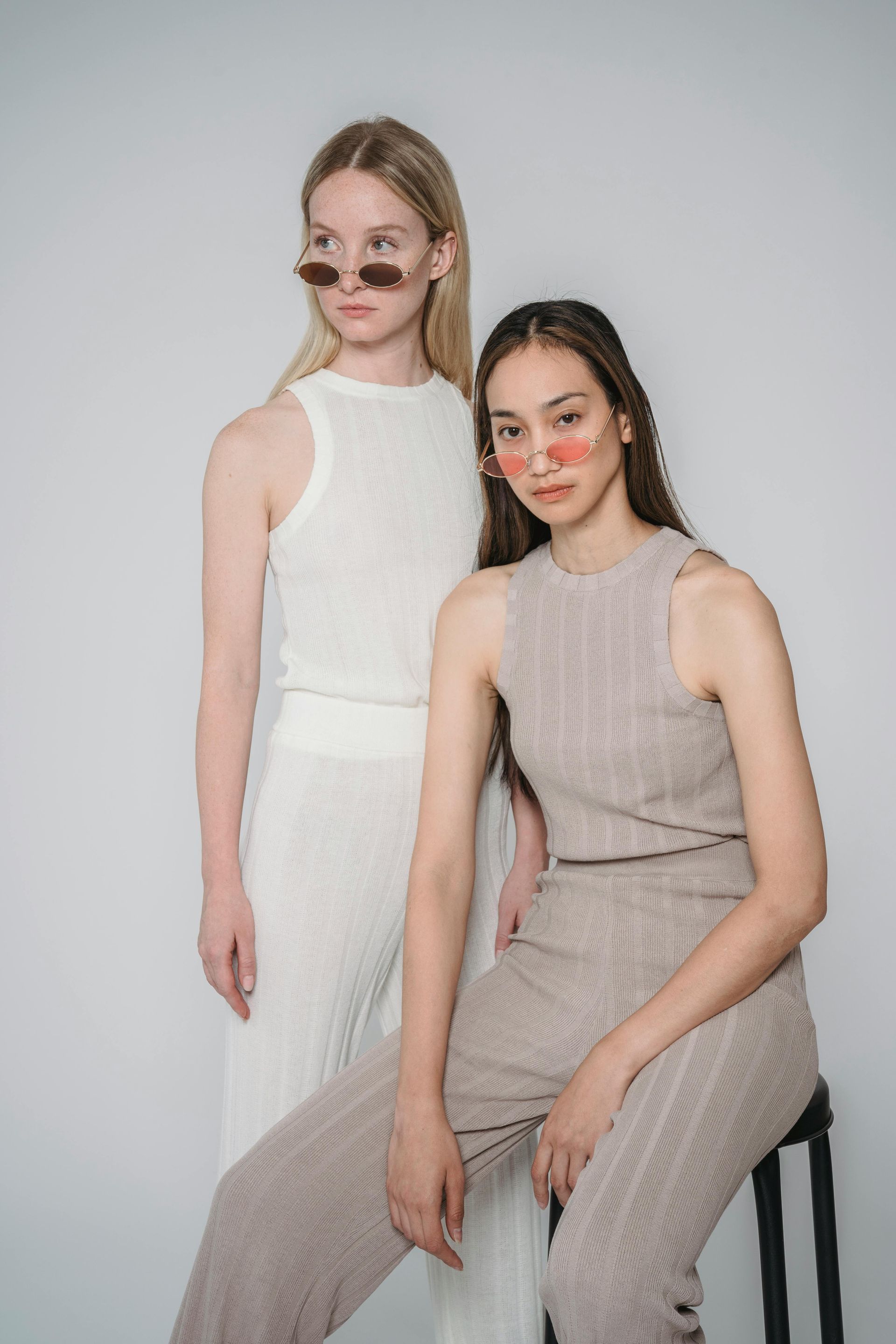 Two women are standing next to each other and one is sitting on a stool.
