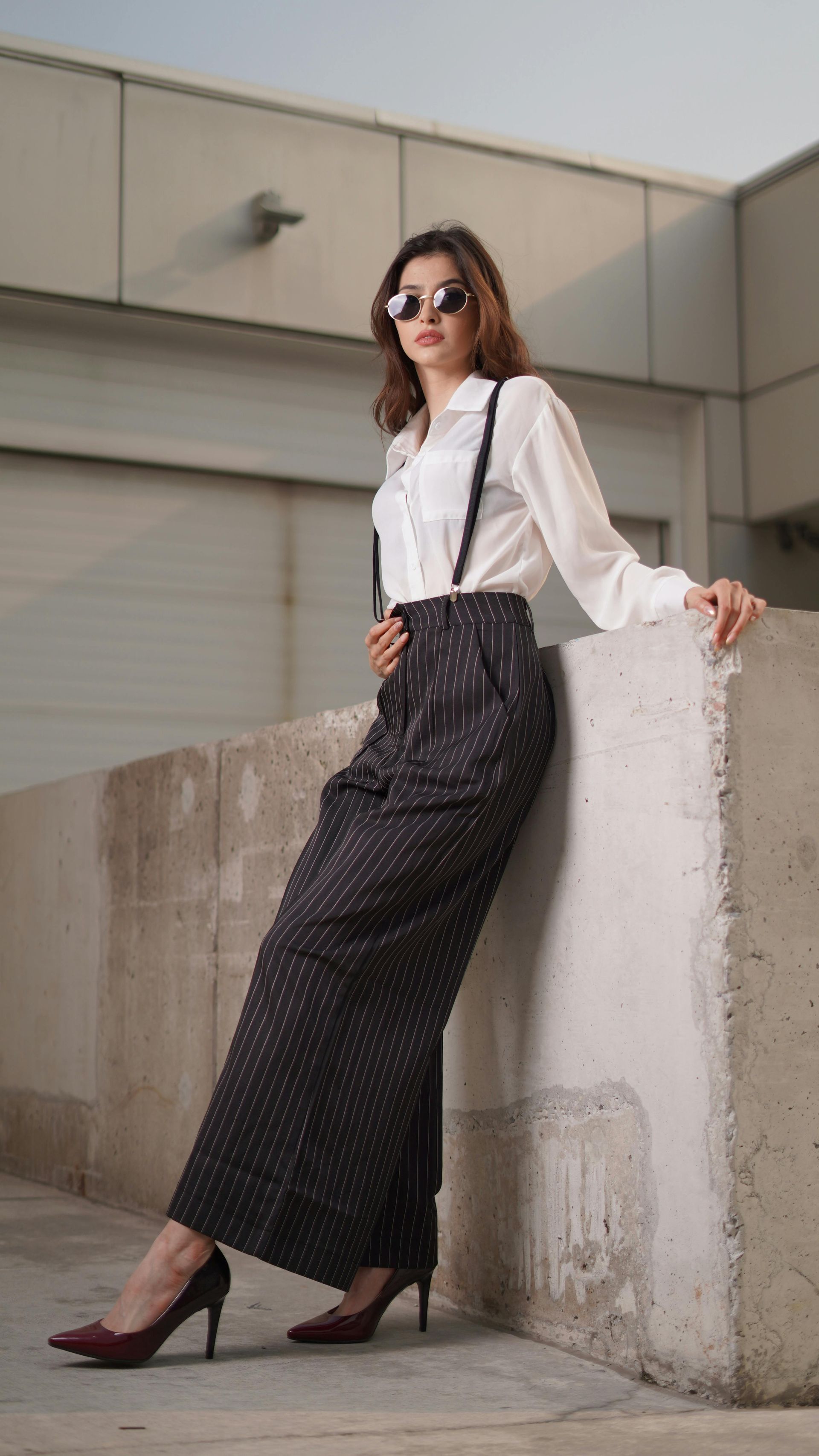 A woman is leaning against a wall wearing a white shirt and black polka dot pants.