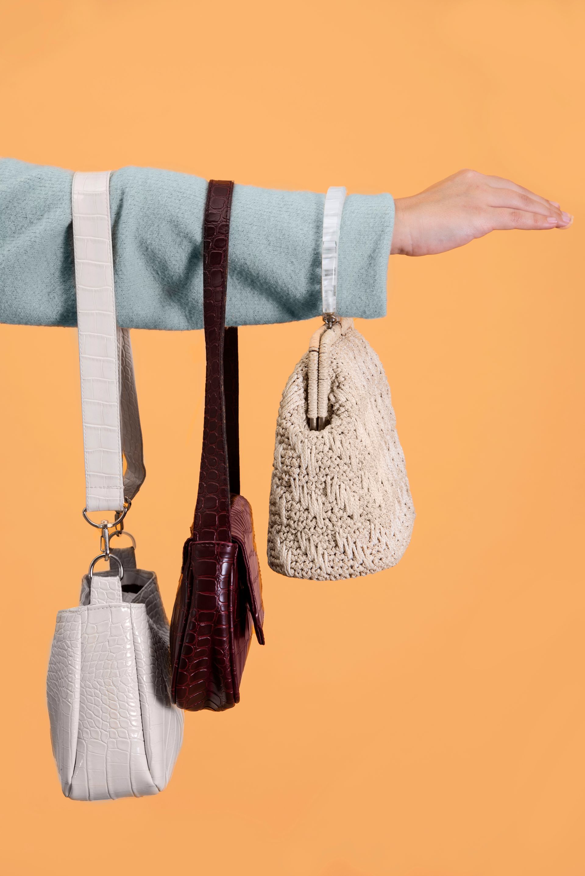 A person is holding three handbags hanging from their arm.