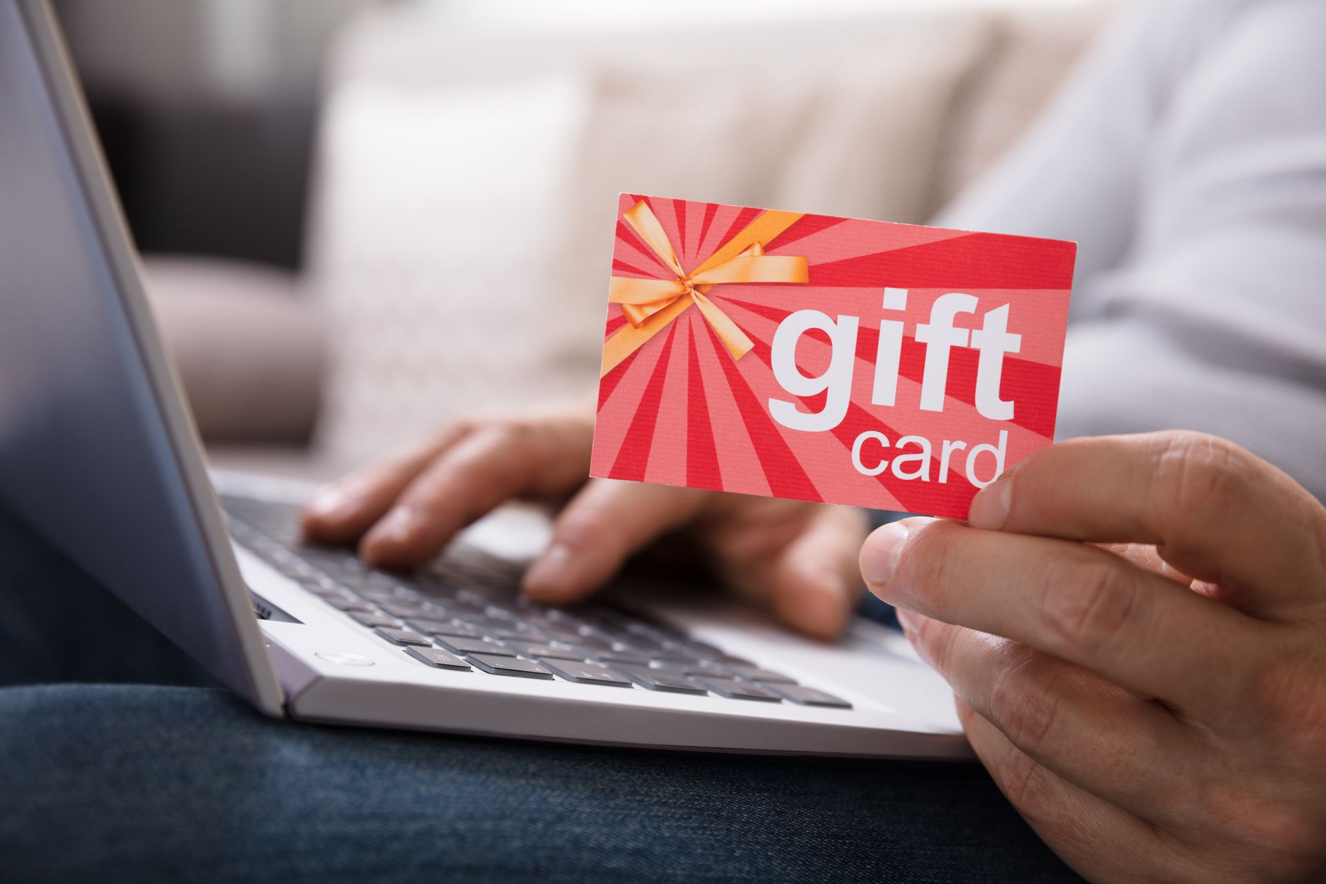A person is holding a gift card in front of a laptop computer.