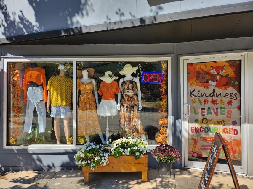 A store front with a window display of clothes and flowers.