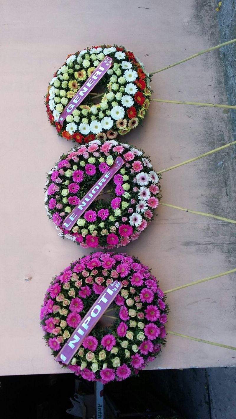 Tre corone di fiori colorati appese con nastri con la scritta