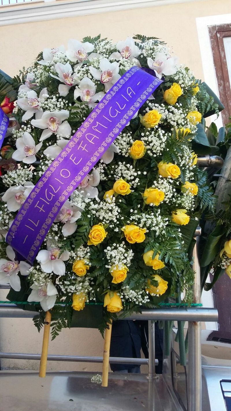 Ghirlanda con orchidee bianche, rose gialle e un nastro viola con la scritta