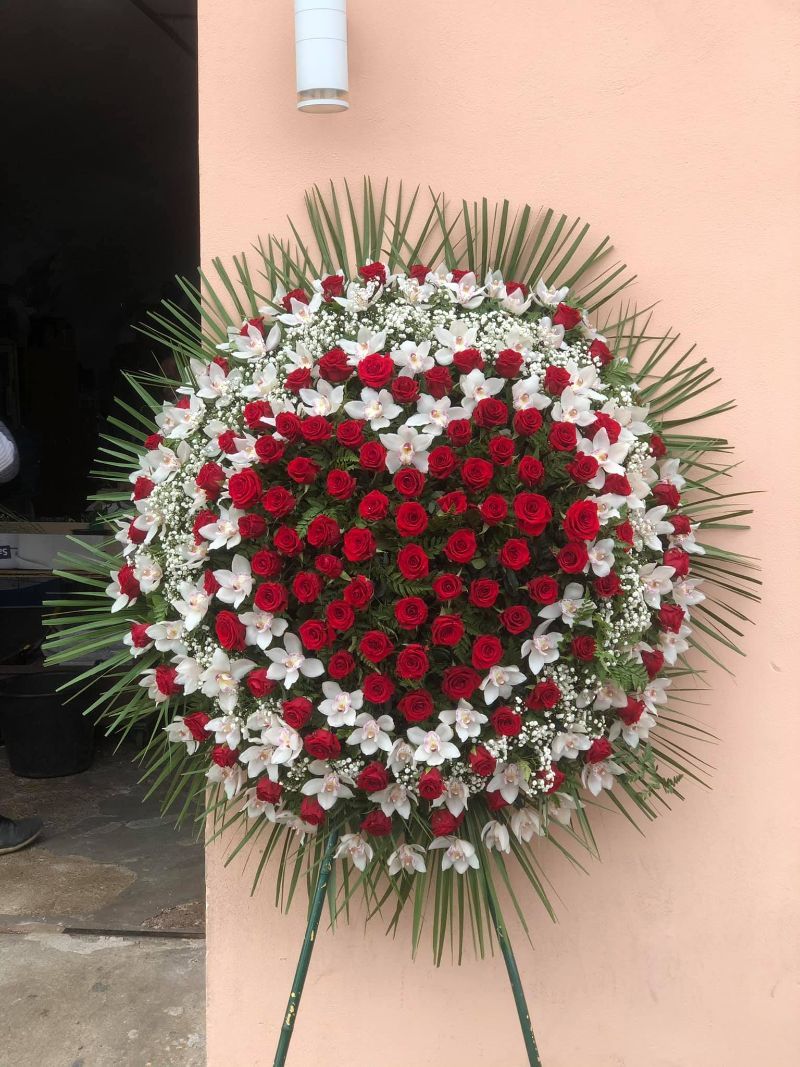 Corona floreale a forma di cuore composta da rose rosse e fiori bianchi su un supporto.