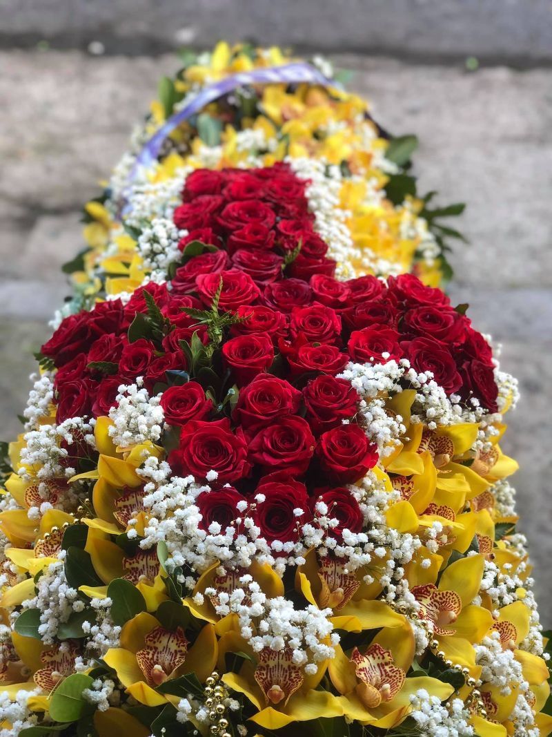 Composizione floreale con una croce di rose rosse circondata da orchidee gialle e dettagli bianchi.