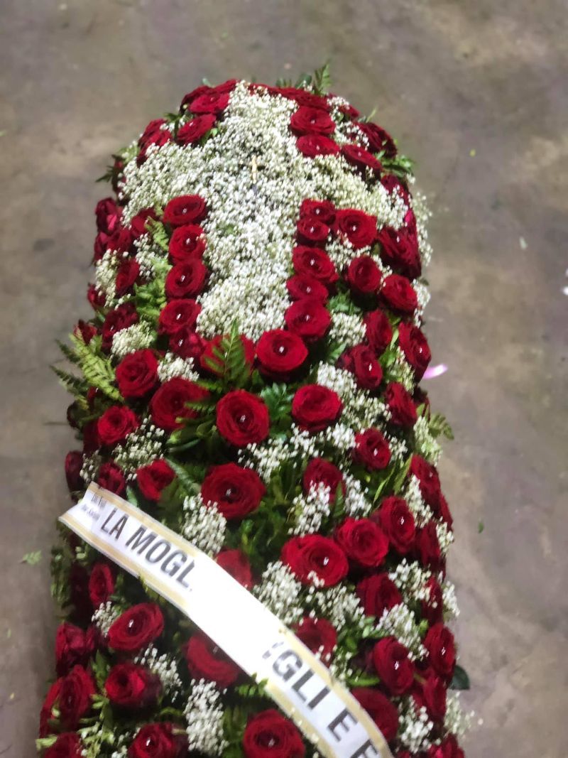 Composizione floreale per funerale: rose rosse e fiori bianchi disposti a croce, con un nastro.