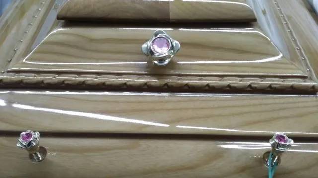 Primo piano di una bara di legno con manici decorativi color gioiello rosa.
