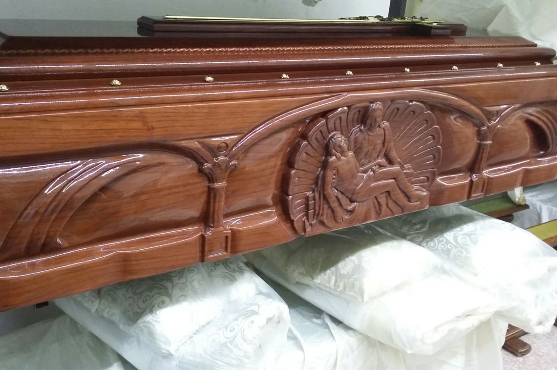 Primo piano di una bara di legno con figure intagliate in rilievo, appoggiata su un tessuto bianco.