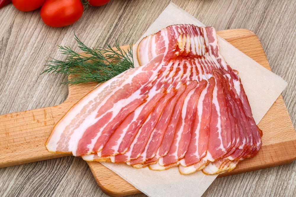 Slices of raw bacon arranged on a wooden cutting board with tomatoes and dill - Drovers Meats in Coffs Harbour, NSW