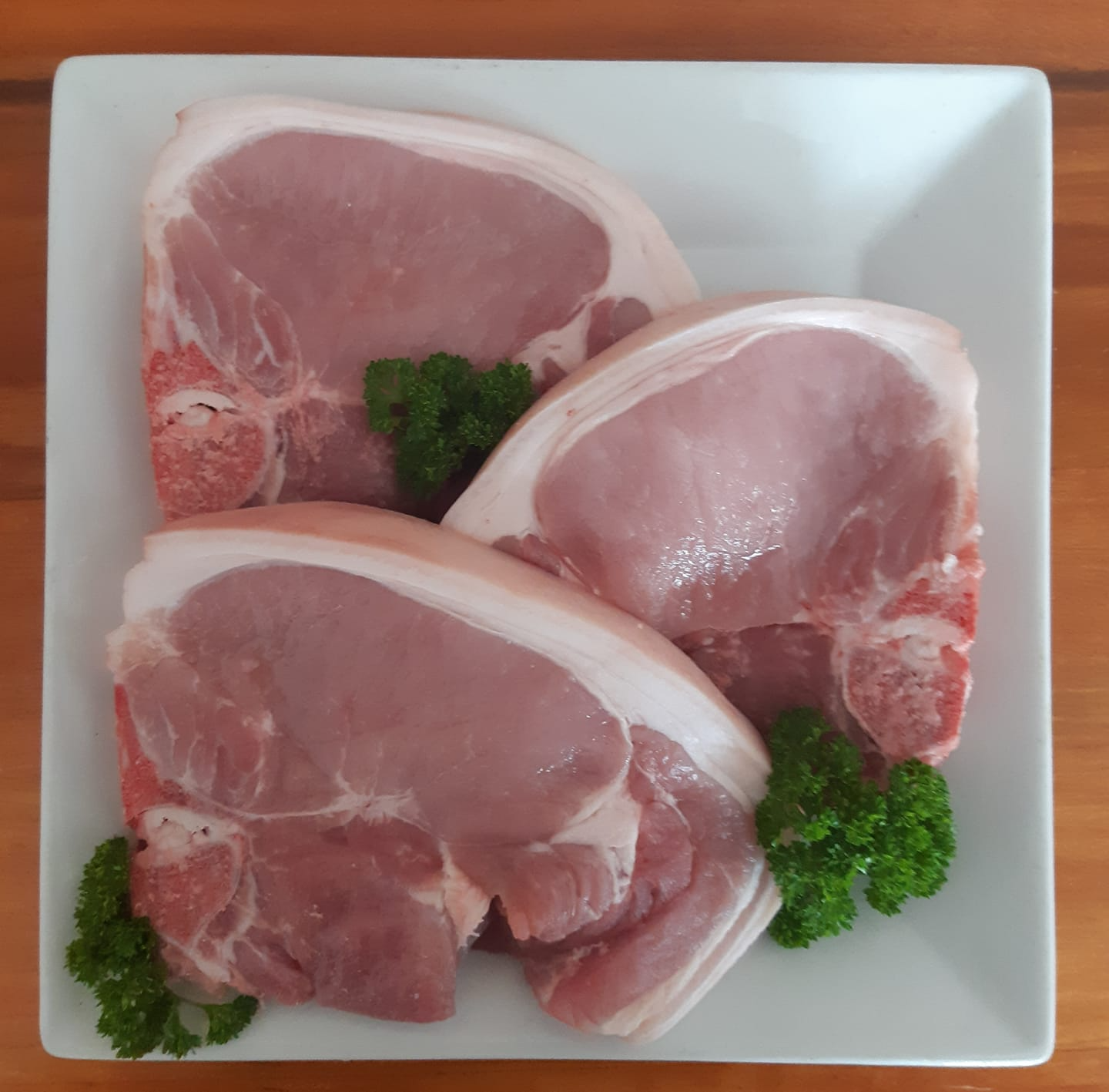Three Raw Pork Chops on a White Square Plate — Drovers Meats in Coffs Harbour, NSW