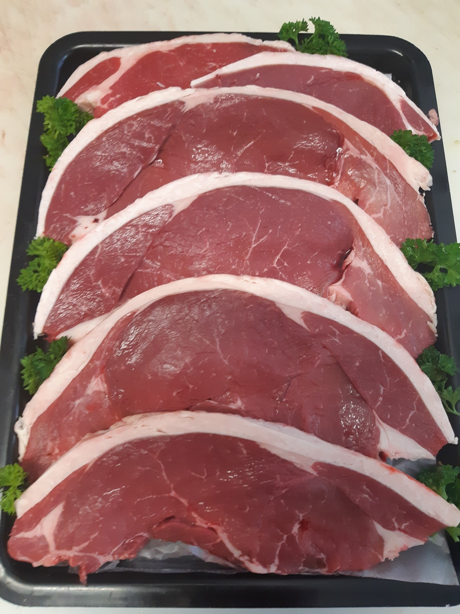 Raw steaks arranged on a black tray with white fat trim and parsley garnish— Drovers Meats in Coffs Harbour, NSW