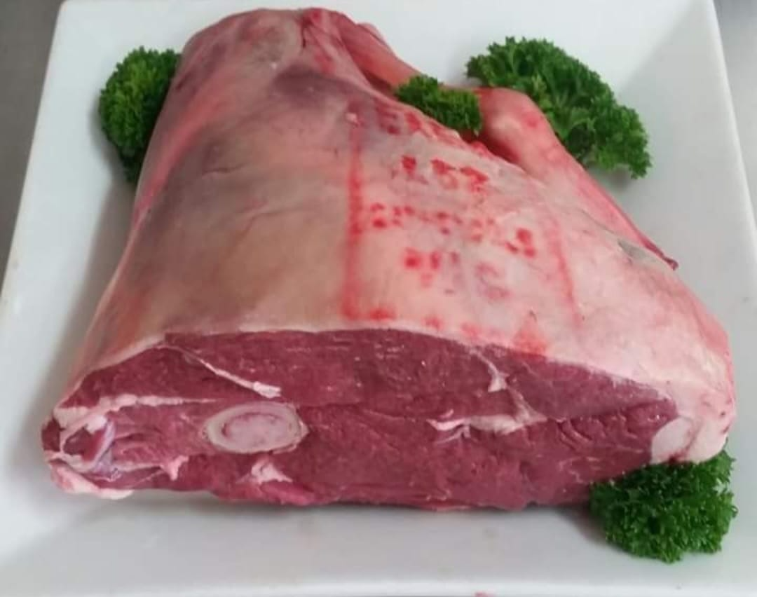 Raw Lamb Leg on a White Plate with Green Garnish — Drovers Meats in Coffs Harbour, NSW