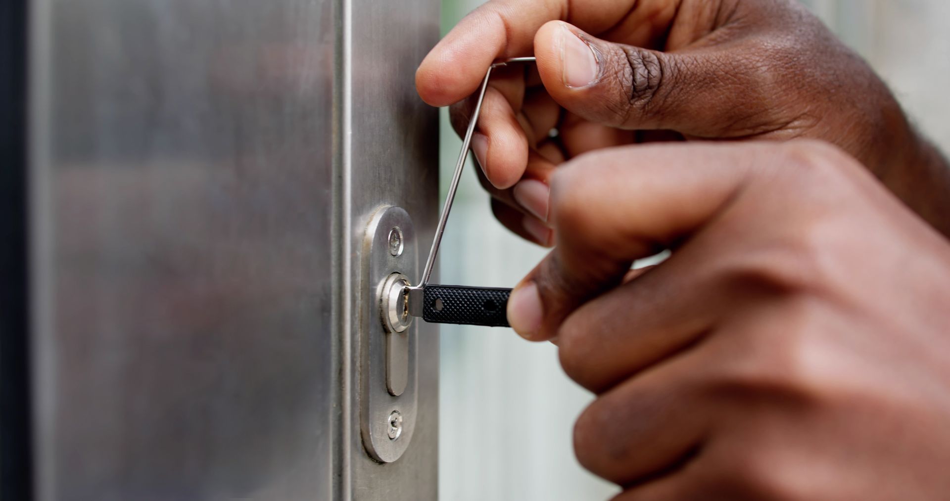 Hands picking a lock with a tension wrench and pick on a metal door