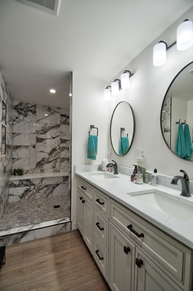 Bathroom with a white double vanity, round mirrors, and a marble-tiled shower.