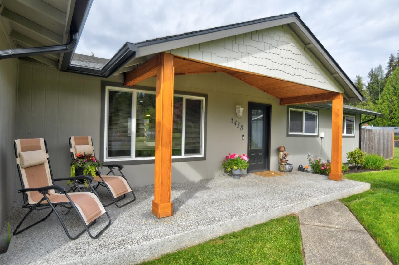 Ranch-style house with gray exterior, covered porch with wood beams, and chairs.