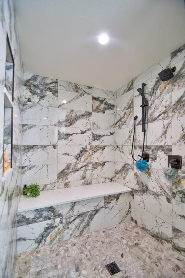 A modern bathroom with marble-tiled shower, built-in bench, pebble floor, and black shower fixtures.