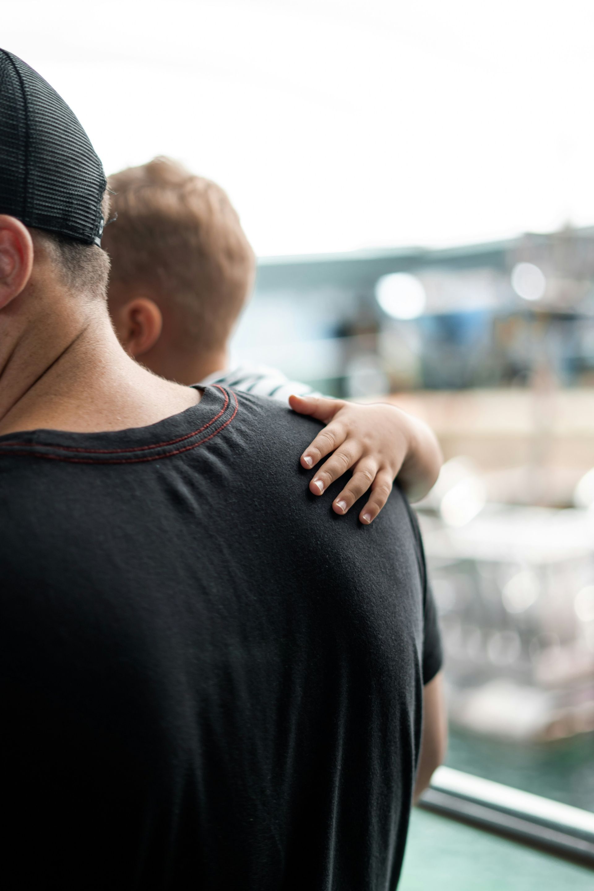 A man is holding a baby on his shoulder while looking out a window.