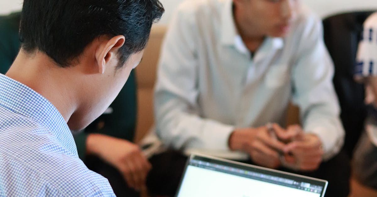 Two men are sitting in front of a laptop computer.