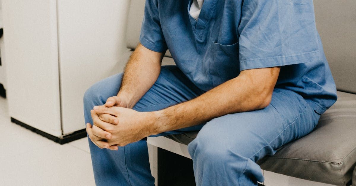 A man in scrubs is sitting on a chair with his legs crossed.