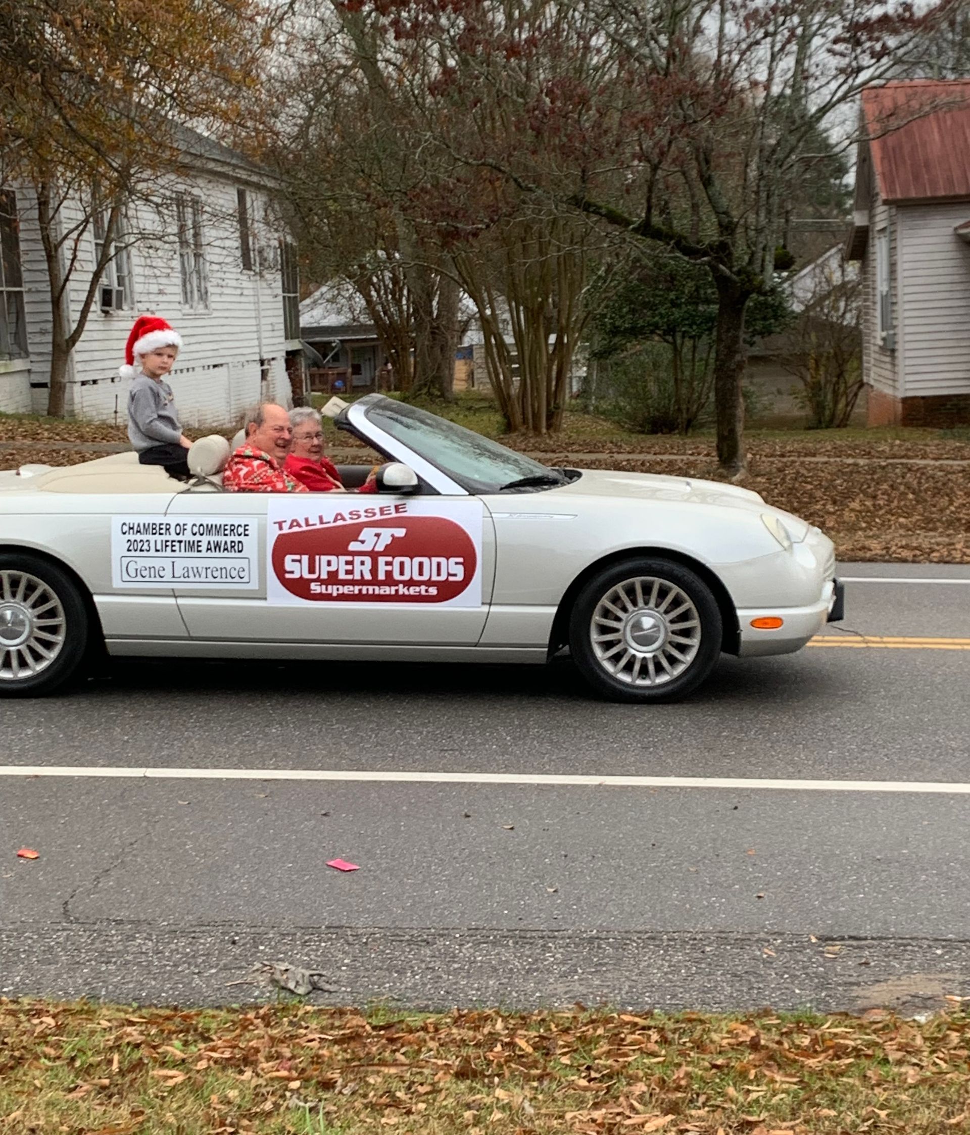 Convertible car in a parade with Santa and a child, banner reads