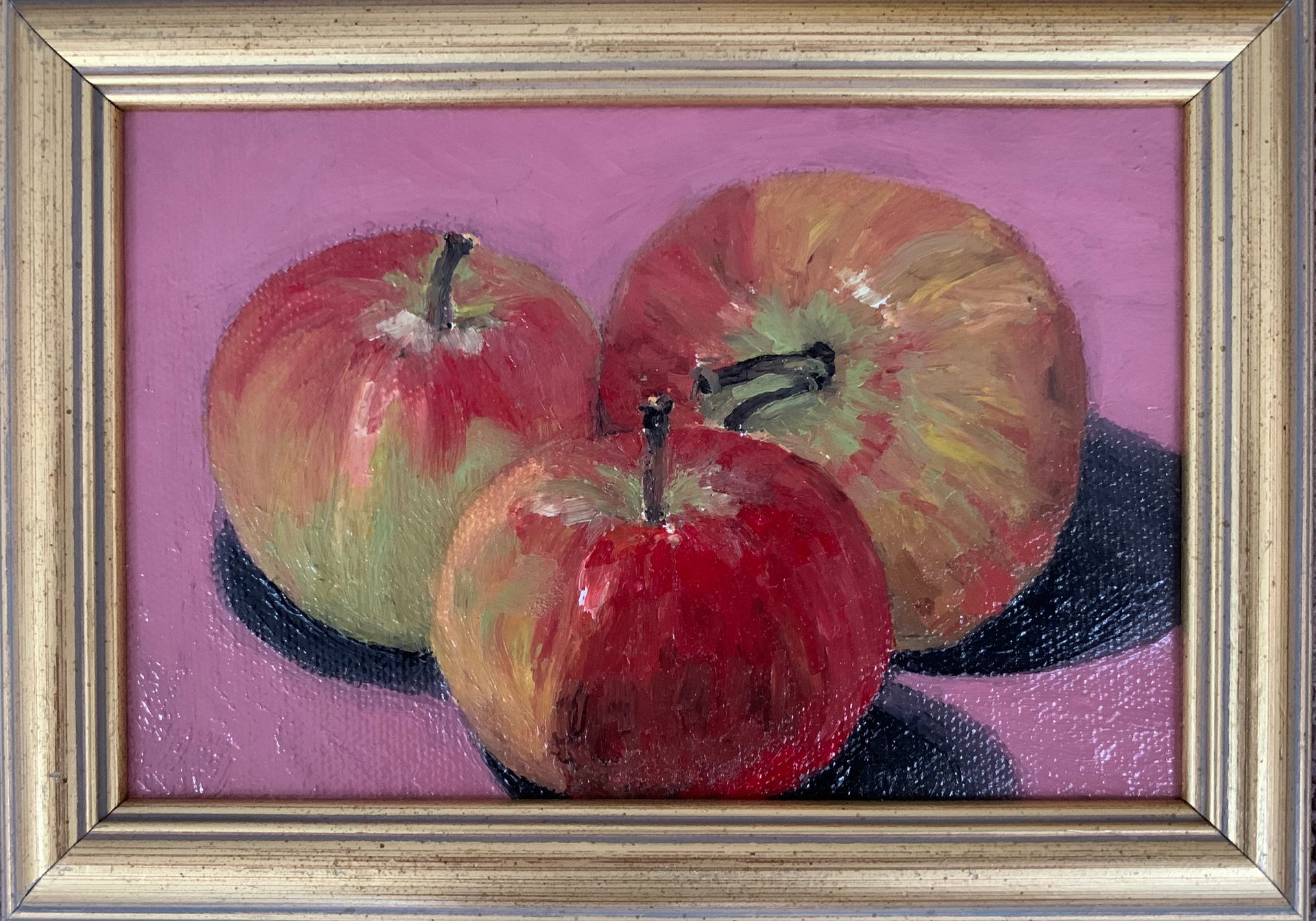 Three apples painted in a gold frame on a pink background