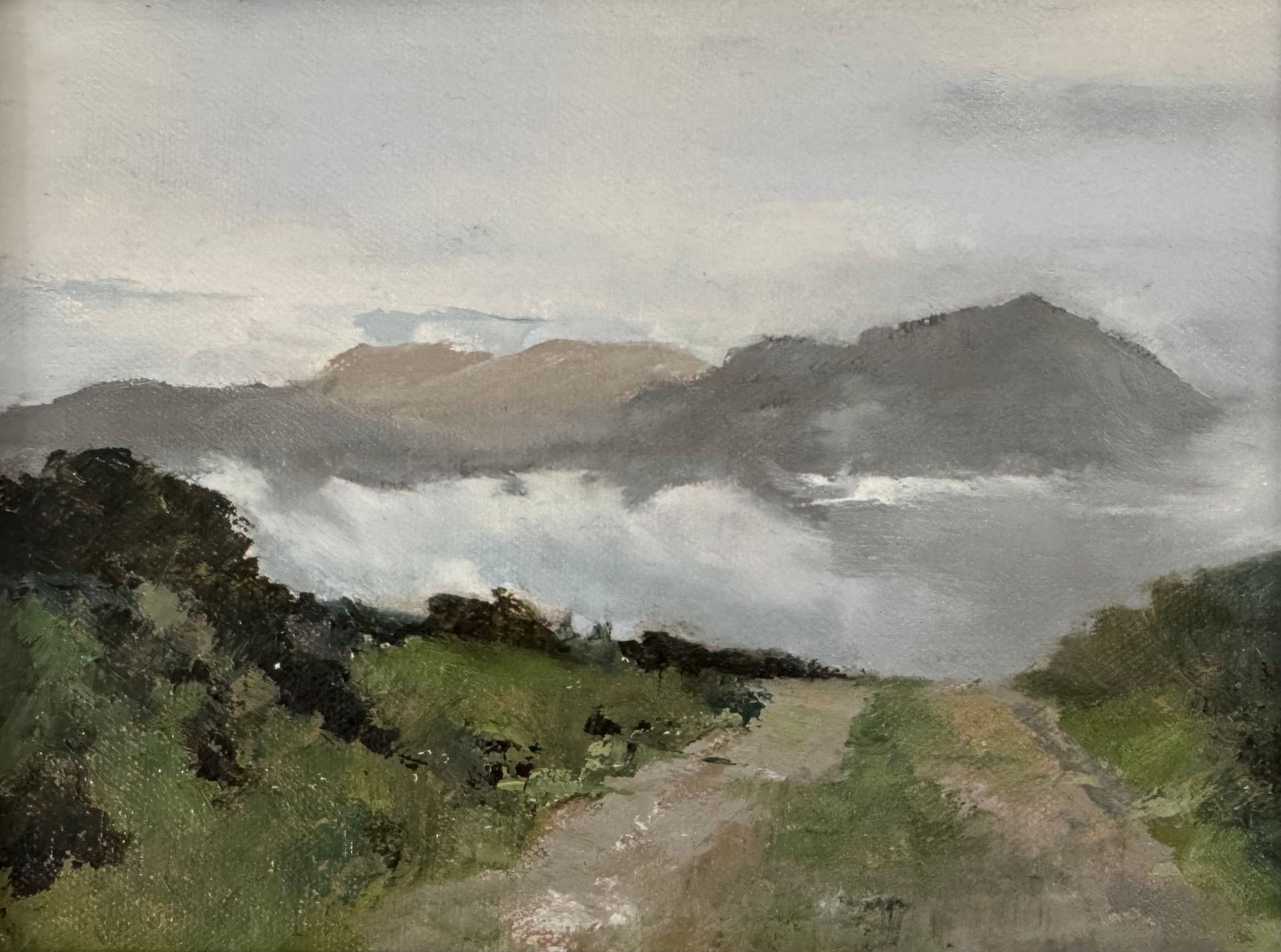 Misty mountain landscape with a dirt road through green hills under a cloudy sky
