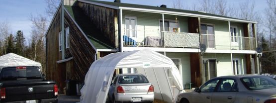 Une maison avec une tente devant et deux voitures garées devant.