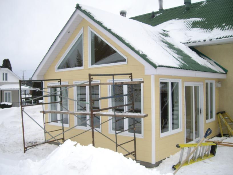 Une maison jaune avec un toit vert est recouverte de neige