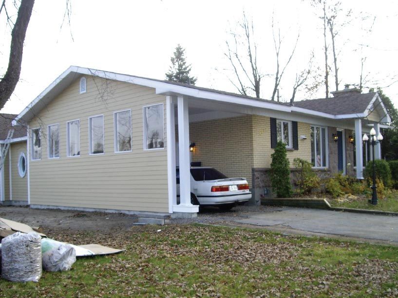 Une voiture blanche est garée sous un porche devant une maison
