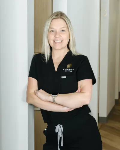 Smiling staff member in black uniform standing with arms crossed in a hallway