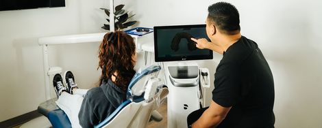 Person in dental chair watching a screen while a clinician points at it in a bright clinic room