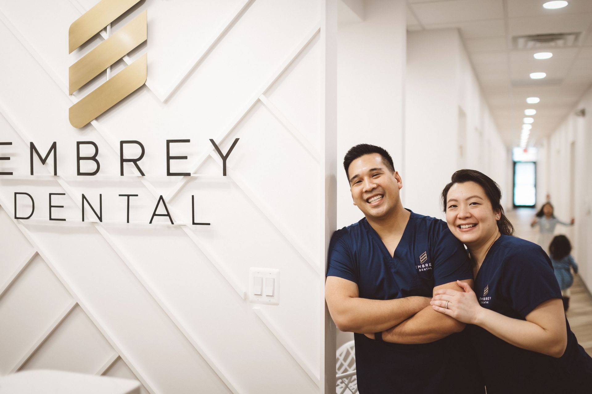 dr lim and office manager rose lim standing by the front of the office logo wall