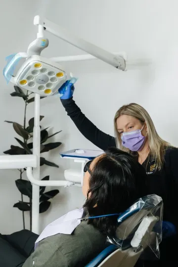 Dentist adjusting overhead light while treating a patient in a dental chair