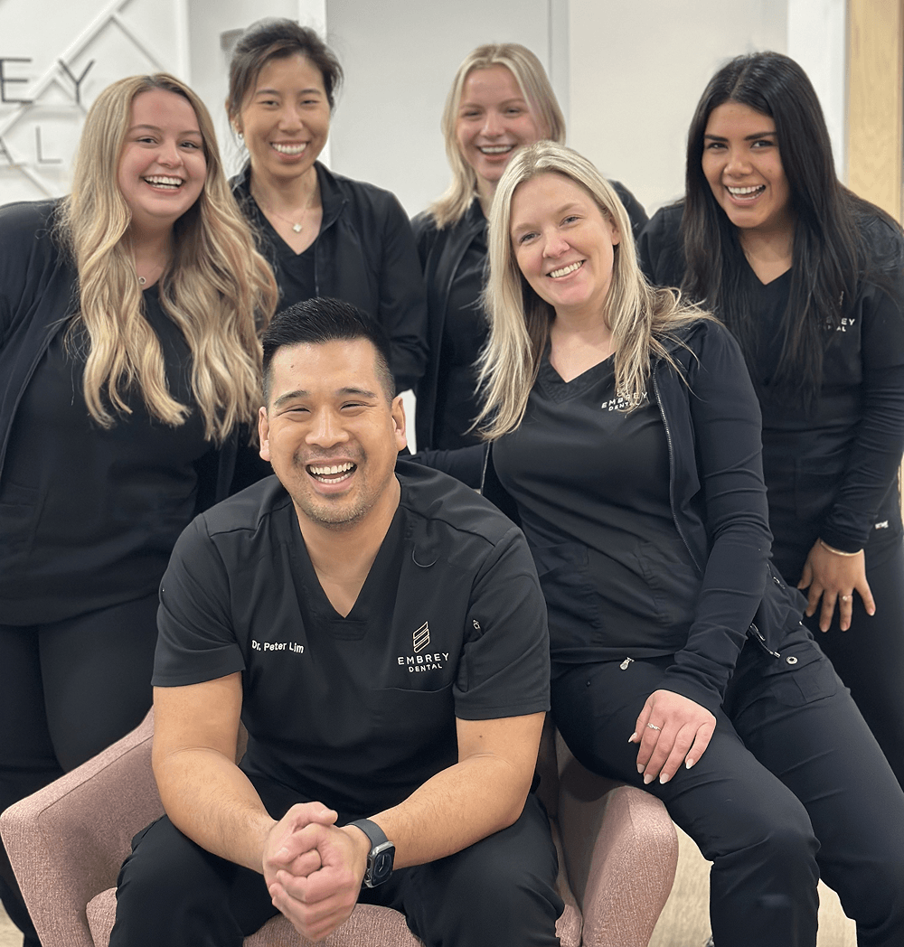 Six smiling coworkers in black uniforms posing together in an office lobby