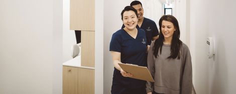 Two smiling people stand in a bright room, holding a clipboard.