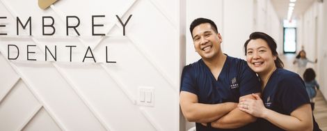 Embrey Dental team smiling in a bright office beside the logo sign