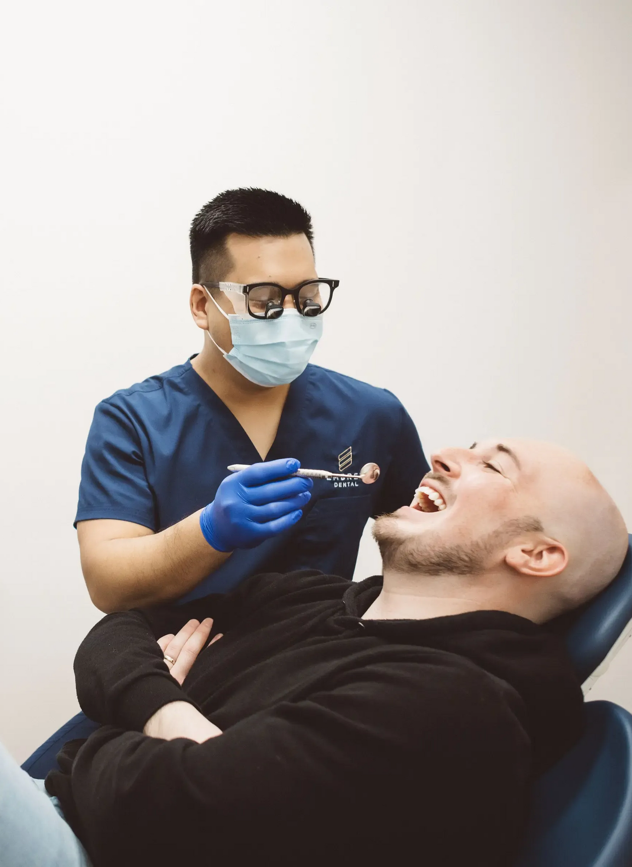 Dentist in blue gloves and mask treating a reclined patient in a clinic chair