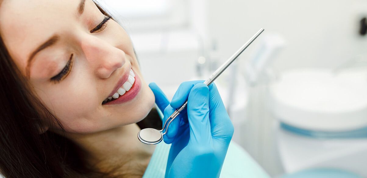 Dental hygienist in blue gloves using a mirror in a patient’s open mouth during a checkup