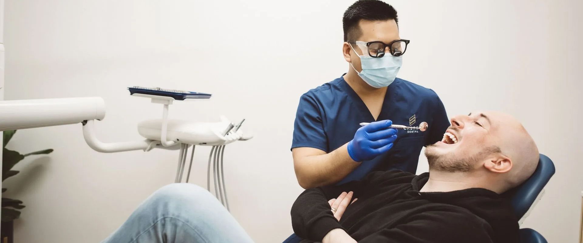 Dentist wearing mask and gloves examining a reclining patient in a dental clinic