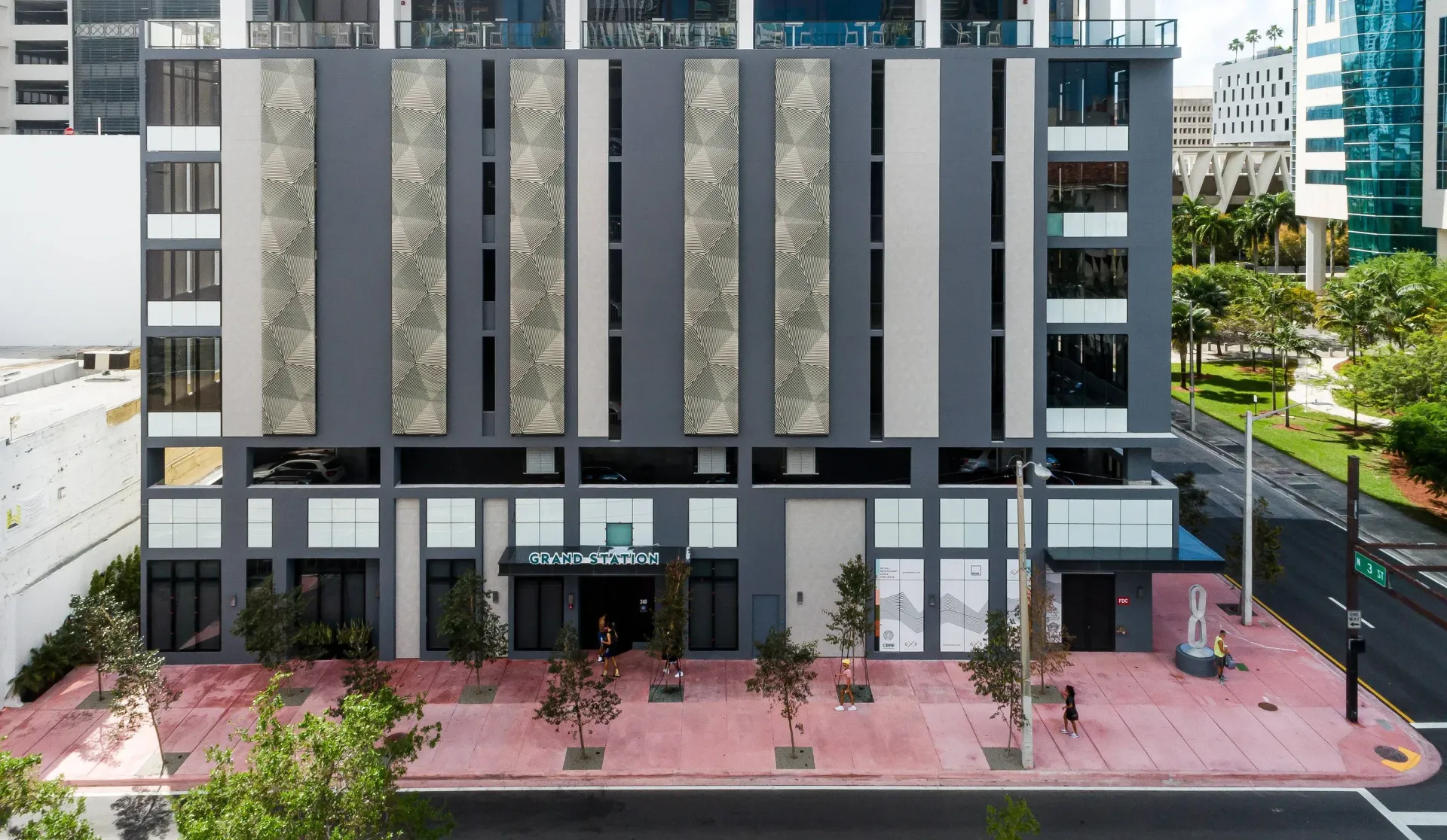 Exterior view of a modern apartment building with a pink sidewalk and Grand Station signage.