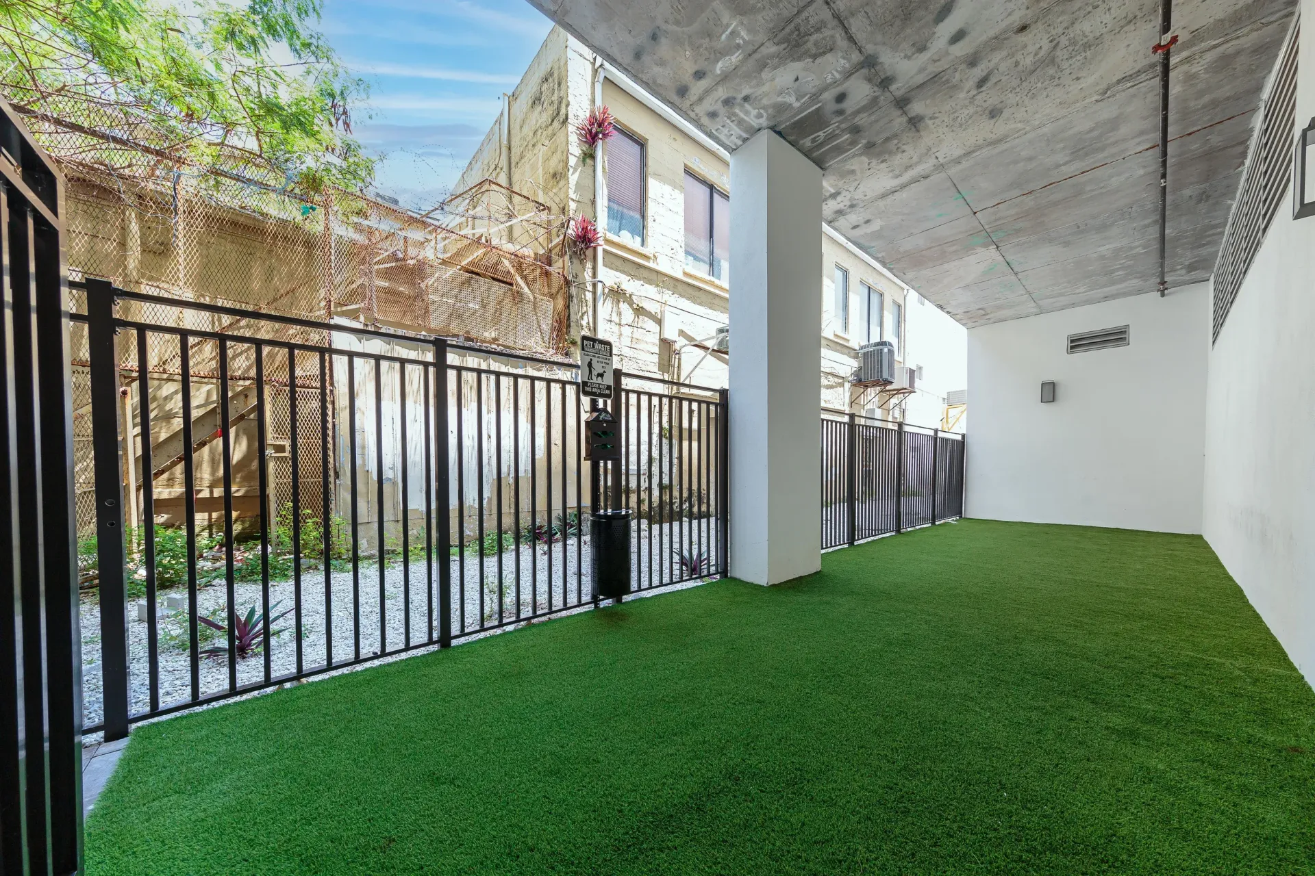 Outdoor community courtyard with artificial turf, black metal fencing, and a concrete ceiling.